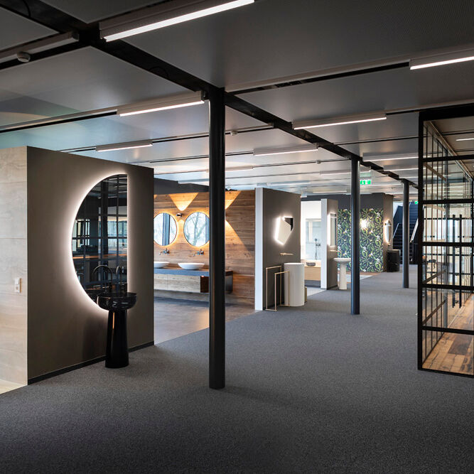 Ausstellungsraum mit verschiedenen Badeinrichtungen. Moderne Designs, beleuchtete Spiegel und stilvolle Waschbecken. Offene, geräumige Gestaltung mit Glaswänden und Holzelementen.