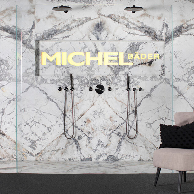 Moderne Dusche mit Marmorwand, zwei Duschköpfen und eleganten Armaturen. Ein Sessel mit Kissen steht daneben. Stilvoll und luxuriös eingerichtet. Moderne Dusche mit Marmorwand, zwei Duschköpfen und eleganten Armaturen. Ein Sessel mit Kissen steht daneben. Stilvoll und luxuriös eingerichtet.