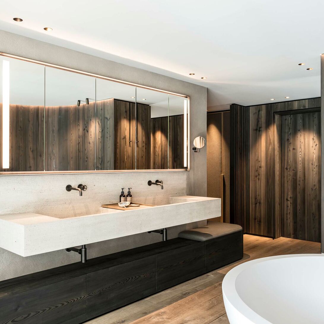 Modernes Badezimmer mit gro&szlig;em Spiegel, Doppelwaschbecken, Holzverkleidung, freistehender Badewanne und eleganter Beleuchtung. Luxuri&ouml;ses Design.