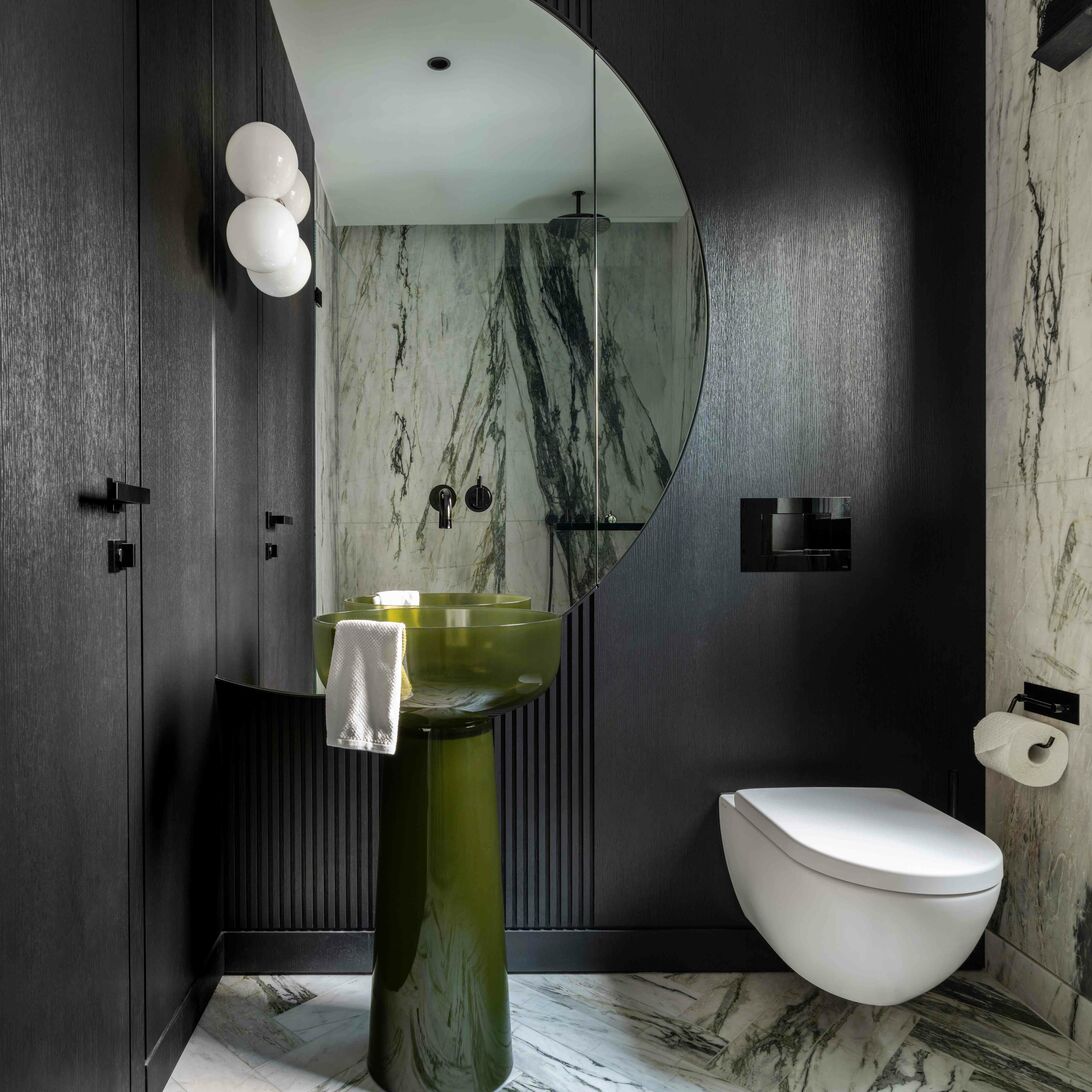 Modernes Bad mit gr&uuml;nem Standwaschbecken, rundem Spiegel, marmorierten W&auml;nden und Boden. Schwarze Akzente und schwebende Toilette vervollst&auml;ndigen das Design.