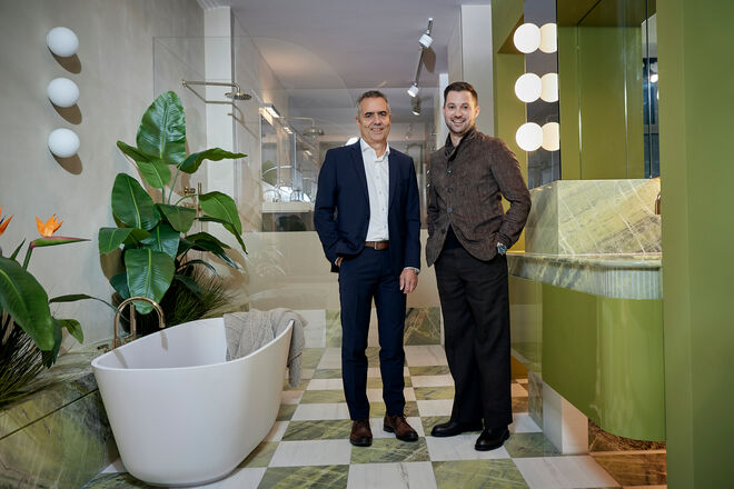 Zwei Männer posieren in einem eleganten Badezimmer mit grünen Akzenten, einer freistehenden Badewanne und großen Pflanzen. Zwei Männer posieren in einem eleganten Badezimmer mit grünen Akzenten, einer freistehenden Badewanne und großen Pflanzen.